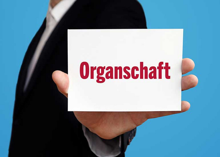 Eine Person mit Anzug hält einen Zettel mit der Aufschrift „Organschaft” in die Höhe.