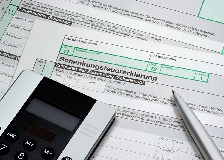 Taschenrechner und Kugelschreiber liegen auf Formularen für eine Schenkungssteuererklärung.