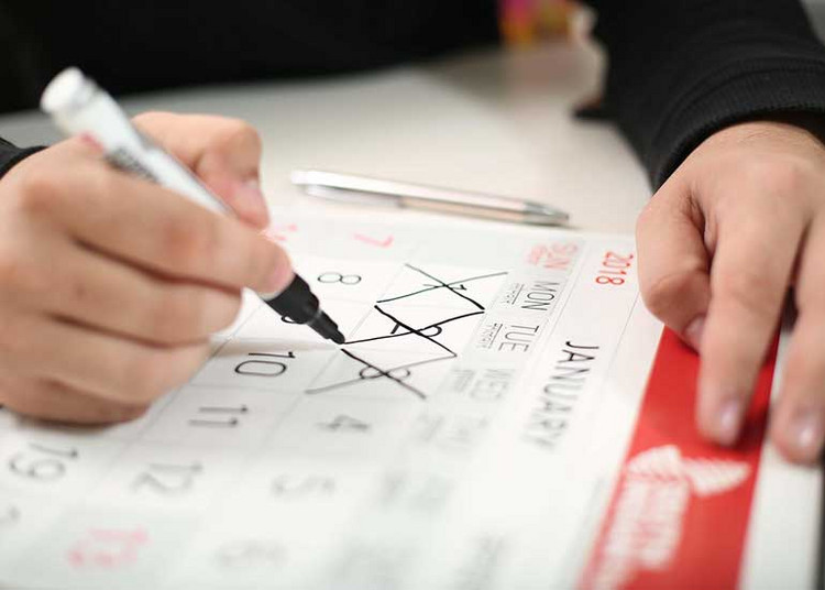 Eine Person sitzt an einem Schreibtisch und durchstreicht Tage auf einem Kalender.