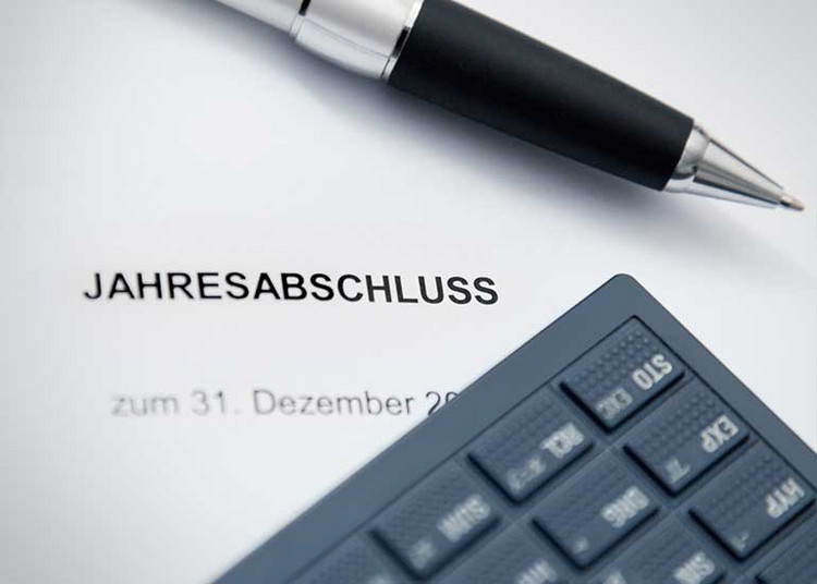 Auf einem Blatt Papier mit der Aufschrift „Jahresabschluss zum 31. Dezember” liegen ein Taschenrechner und ein Kugelschreiber.