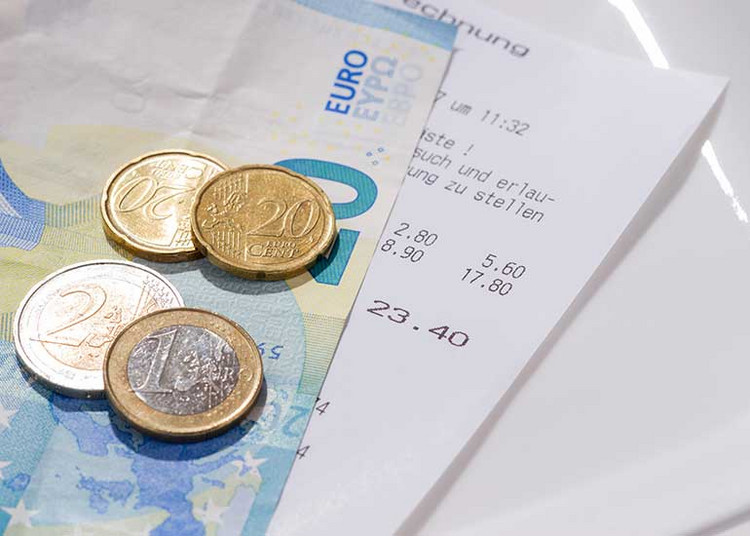 Auf einem Tisch liegen ein Rechnungsbeleg sowie Euro-Banknoten und -Münzen.