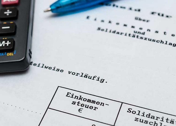 Auf der Einkommensteuererklärung liegen ein Taschenrechner und ein Kugelschreiber.