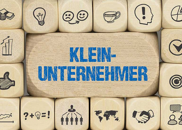 Ein großer Baustein mit der Aufschrift „Kleinunternehmer“. Darum herum liegen kleinere Bauklötze mit Symbolen wie z.B. Handschlag, Geldscheine und Münzen, einem Pfeil in der Mitte einer Zielscheibe und Glühbirnen.