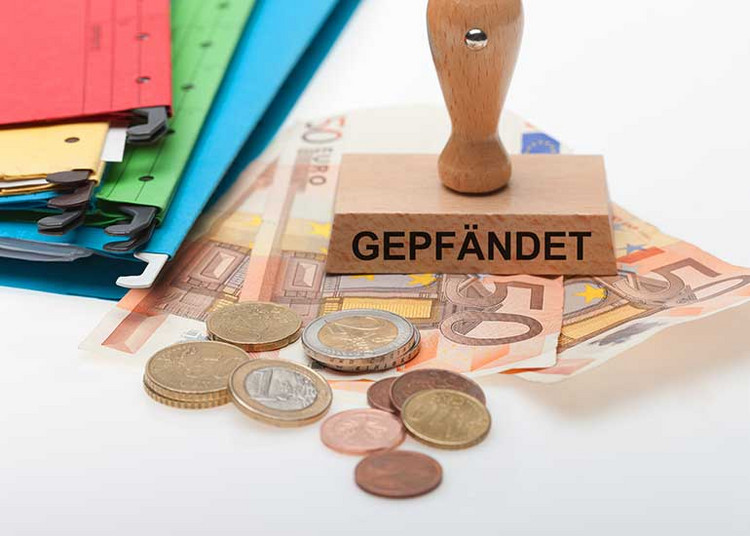 Auf Euro-Banknoten steht ein Stempel mit der Aufschrift „gepfändet”. Daneben liegen Ordner und Euro-Münzen.