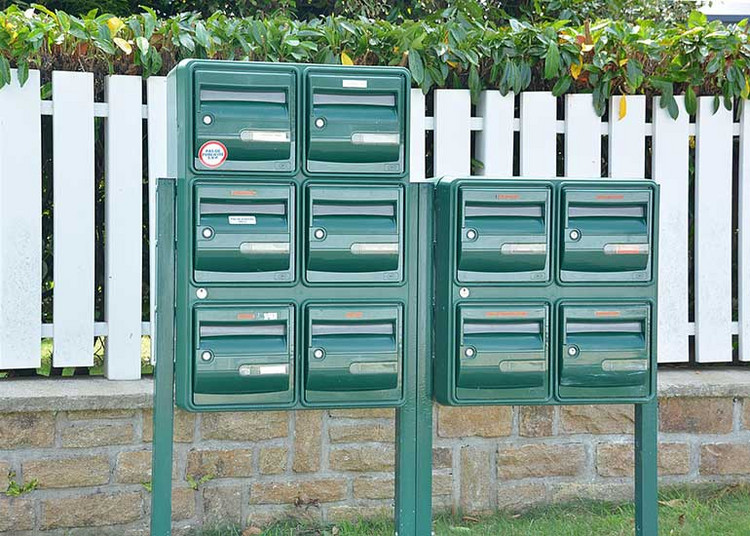 Vor einem Gartenzaun stehen mehrere Briefkästen.