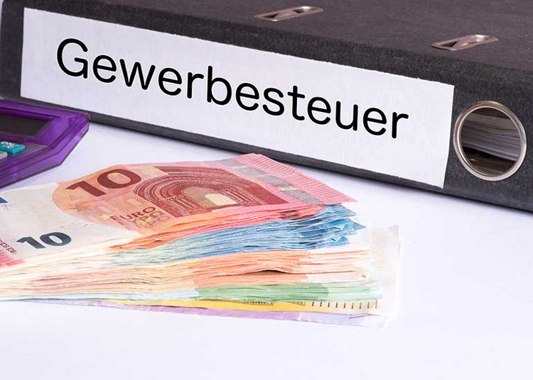 Ein Aktenordner mit der Aufschrift „Gewerbesteuer” liegt neben Euro-Banknoten und einem Taschenrechner.