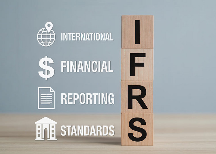 Die Bildcollage zeigt vier Holzklötze, auf denen jeweils ein Buchstabe des Begriffs „IFRS” zu sehen ist. Daneben steht jeweils die Erklärung zur Abkürzung. I steht für International, F für Financial, R für Reporting und S für Standards. Zudem sind den Begriffen Symbole zugeordnet. Dies sind eine Weltkugel für „International”, ein Dollarzeichen für „Financial”, ein Dokument für „Reporting” und ein Haus für „Standards”.