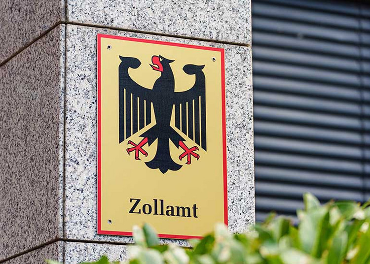 Zu sehen ist die Fassade eines Hauses. Auf einer Säule befindet sich ein Schild mit der Aufschrift „Zollamt” und der Abbildung eines Adlers. 