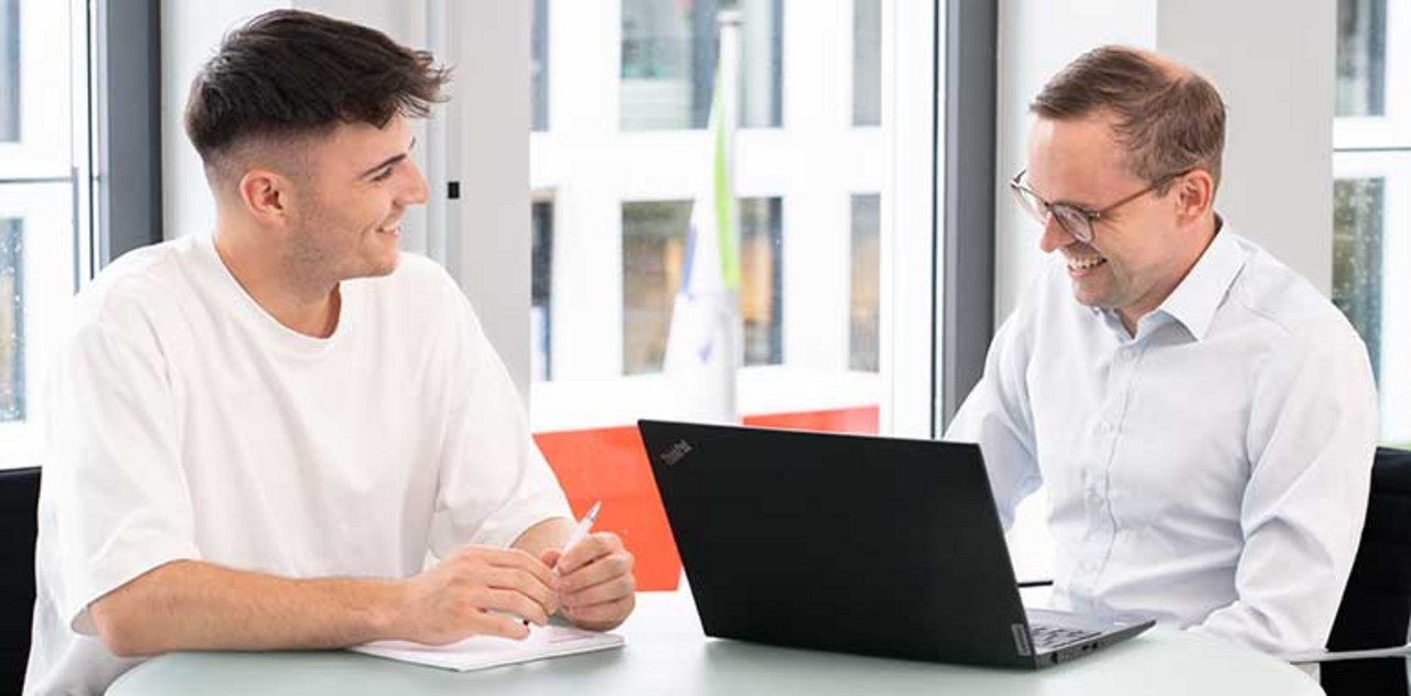 Zwei Personen sitzen mit einem Laptop an einem Tisch.