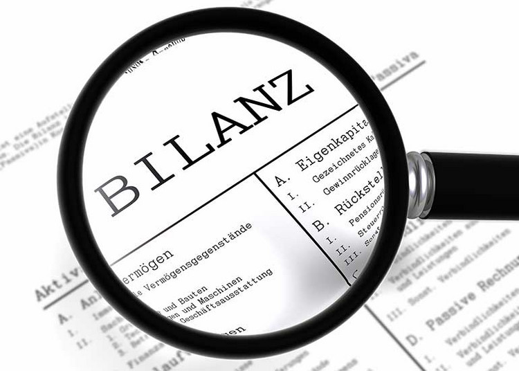 Eine Lupe vergrößert das Wort "Bilanz" auf einem Blatt Papier.