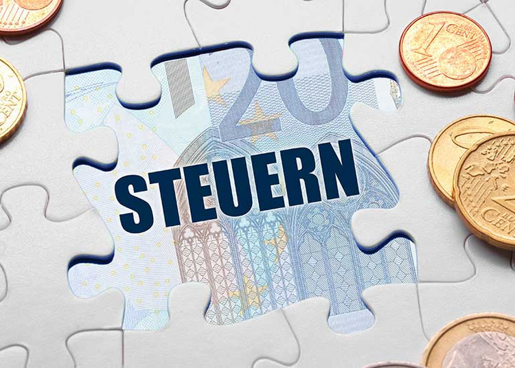 Aus einem Puzzle fehlt ein Teil. Darunter ist der Begriff „Steuern” zu lesen und eine Euro-Banknote zu erkennen. Daneben liegen Euro-Münzen.