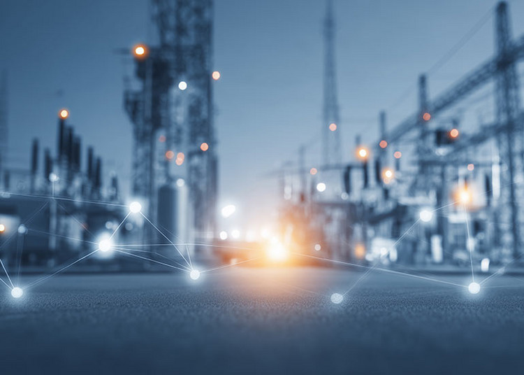 Unscharfe Ansicht eines industriellen Energie- oder Umspannwerks mit technischen Anlagen und Masten. Im Vordergrund sind leuchtende, digital wirkende Verbindungspunkte zu sehen, die ein Netzwerk symbolisieren.