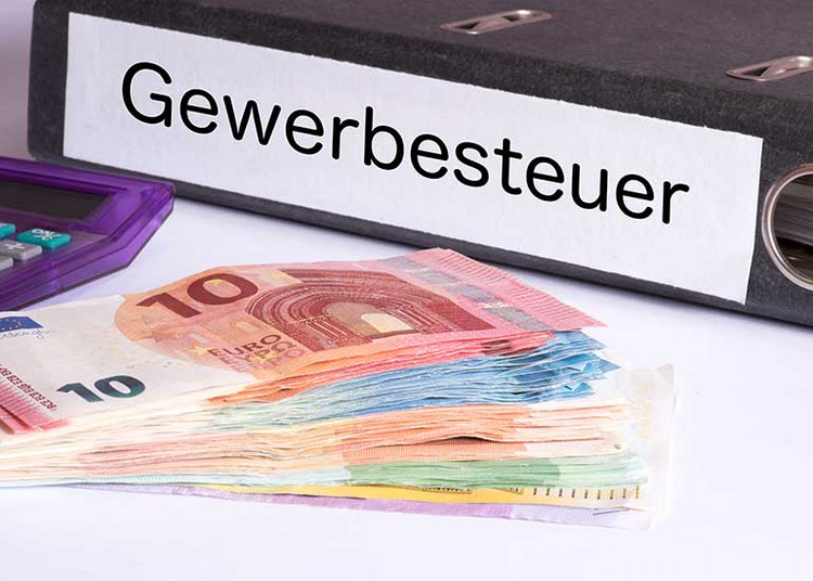 Ein Aktenordner mit der Aufschrift „Gewerbesteuer” liegt neben Euro-Banknoten und einem Taschenrechner.