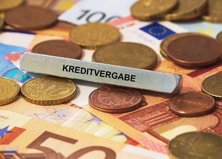 Auf einem Tisch liegen Euro-Banknoten und -Münzen. Darauf steht ein Schild mit der Aufschrift „Kreditvergabe”.