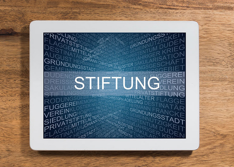 Auf einem Tablet ist der Text „Stiftung” geschrieben. Dahinter sind viele Begriffe wie Rendite, Privatrecht und Kloster angeordnet, die damit in Zusammenhang stehen.