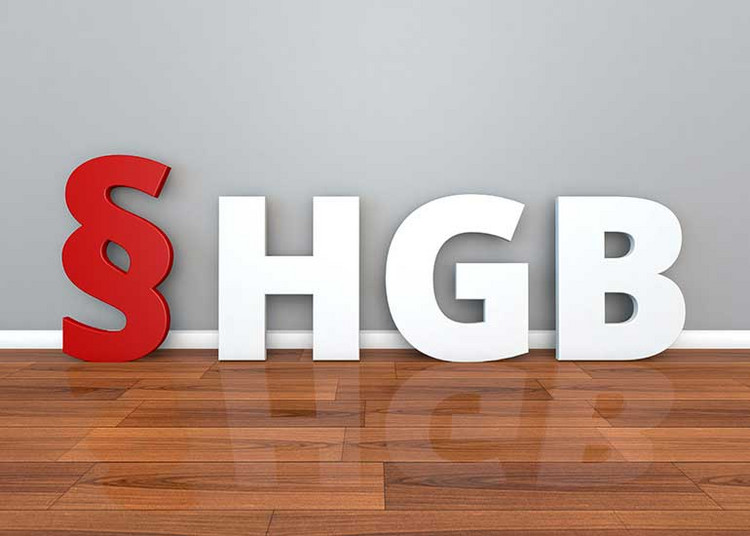 Die Buchstaben „§HGB” stehen auf einem Pakettboden vor einer Wand.