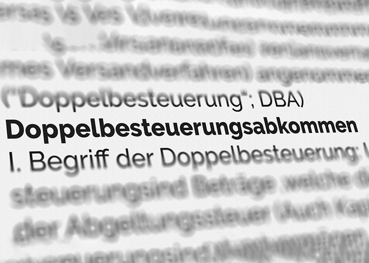 Aufsicht auf eine Seite eines Lexikons. Der Text „Doppelbesteuerungsabkommen“ ist hervorgehoben, der Rest ist weitgehend unscharf.
