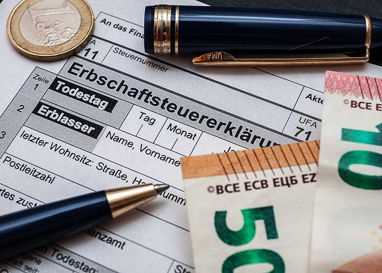 Zu sehen ist eine Erbschaftssteuererklärung, auf der ein Kugelschreiber und Euro-Banknoten liegen.