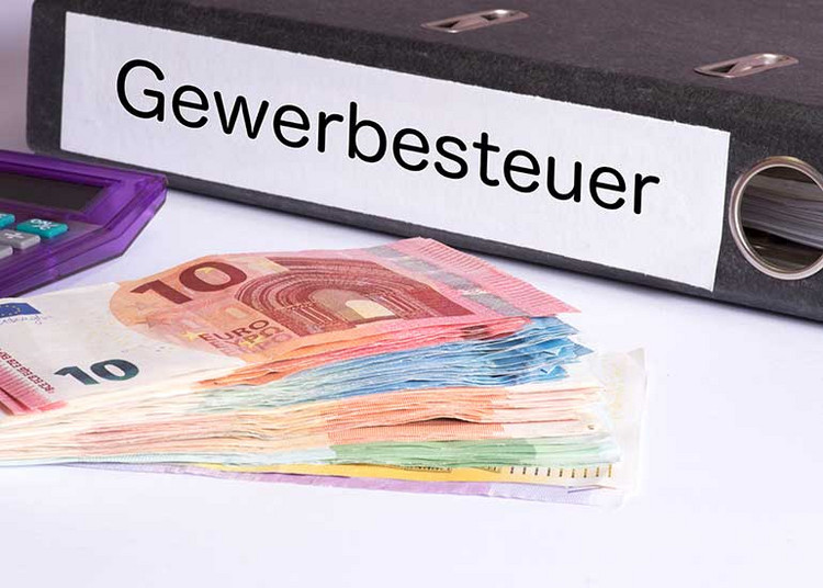 Ein Aktenordner mit der Aufschrift „Gewerbesteuer” liegt neben Euro-Banknoten und einem Taschenrechner.