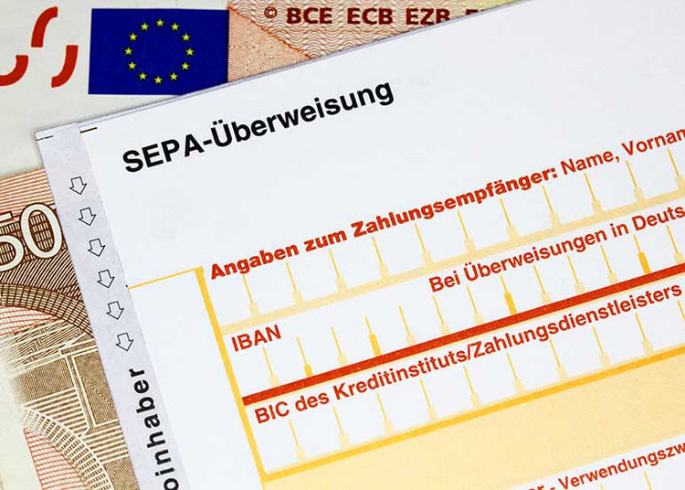 Detailansicht auf eine SEPA-Überweisungsformular darunter liegen Euro-Banknoten.