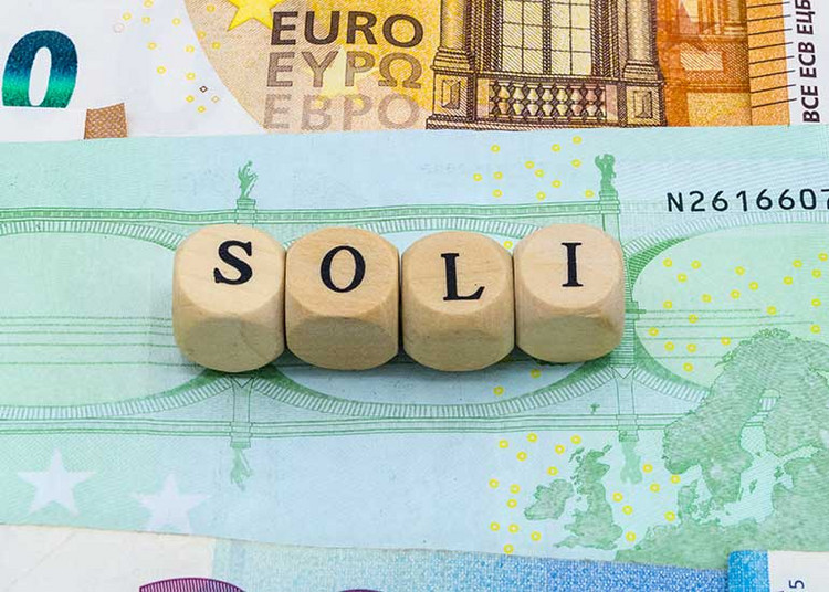 Auf vier Würfeln steht "Soli". Jeder Buchstabe steht auf einem Würfel. Die Würfel stehen auf Euroscheinen.