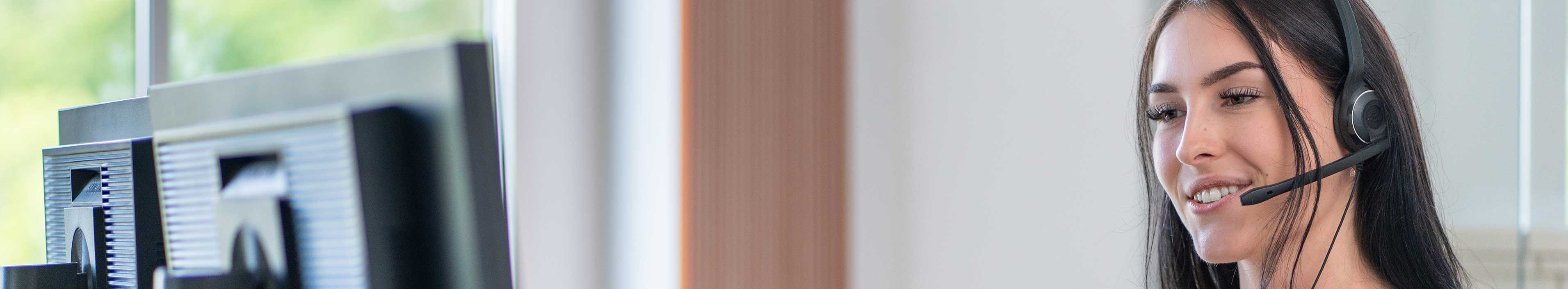 Person sitzt mit einem Headset vor zwei Monitoren.