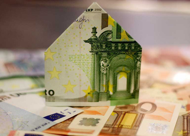 Euro-Banknoten liegen auf einem Tisch. Ein Schein ist zu einem Haus gefaltet und steht über den Scheinen.