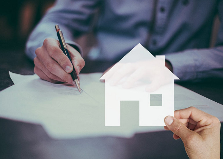 Die Bildcollage zeigt eine Person, die an einem Schreibtisch sitzt und mit einem Kugelschreiber auf Papiere schreibt. Im Vordergrund hält eine weitere Person ein Papier in Form eines Hauses hoch.