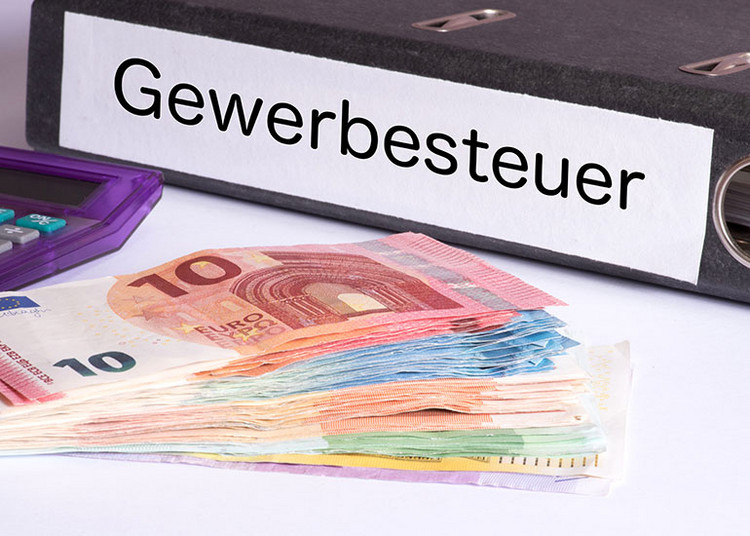 Ein Aktenordner mit der Aufschrift „Gewerbesteuer” liegt neben Euro-Banknoten und einem Taschenrechner.
