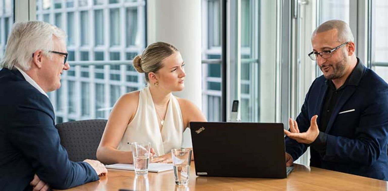 Nexia GmbH | Köln Drei Personen sitzen gemeinsam an einem Tisch und unterhalten sich.