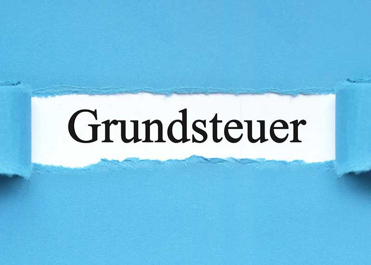 Aus einem Blatt Papier wurde ein Teil herausgerissen. Darunter wird der Text „Grundsteuer” sichtbar.