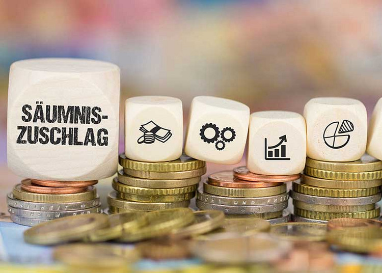 Auf einem Würfel steht „Säumniszuschlag“. Daneben liegen Würfel mit Steuersymbolen. Die Würfel liegen auf Münzstapeln.