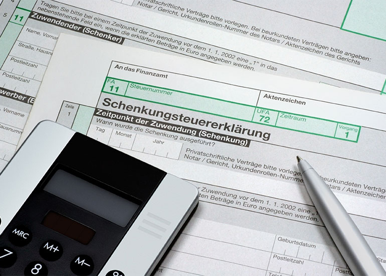 Taschenrechner und Kugelschreiber liegen auf Formularen für eine Schenkungssteuererklärung.