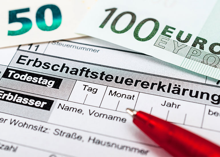 Ein Kugelschreiber liegt auf einer Erbschaftssteuererklärung. Daneben liegen Euro-Banknoten.