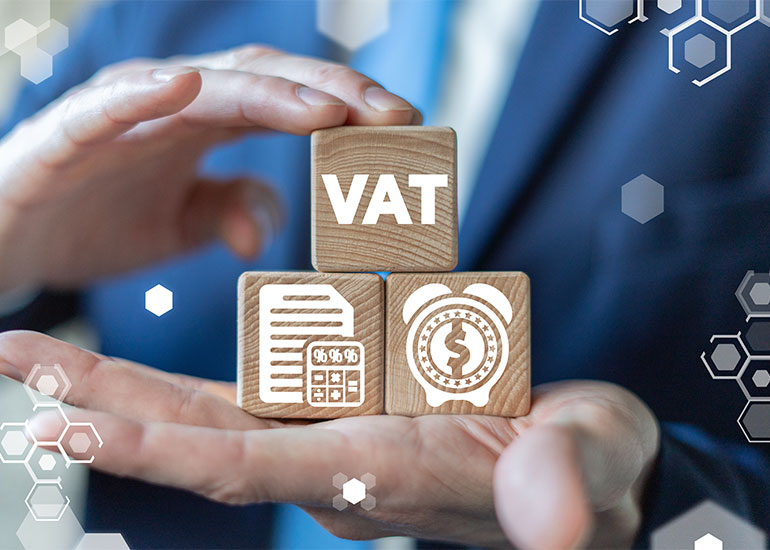 Hand hält drei Bauklötze mit den Symbolen wie "VAT" für Mehrwertsteuer, ein Dokument und ein Wecker.