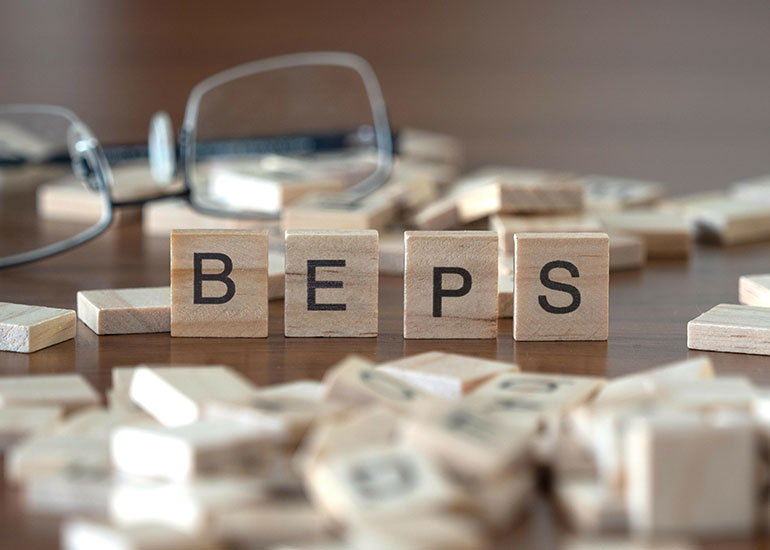 Der Begriff "BEPS" steht für Base Erosion and Profit Shifting. Die Buchstaben "BEPS" stehen jeweils auf einem Holzwürfel auf einem Tisch. Daneben liegen weitere Holzwürfel. Im Hintergrund liegt eine Brille.