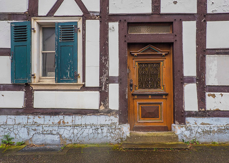Man sieht die Eingangstür eines Fachwerkhauses. Das Haus sieht renovierungsbedürftig aus.