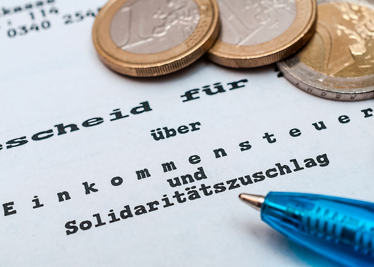 Abgebildet ist ein Ausschnitt auf eine Einkommensteuer.  Darauf liegen Euromünzen und ein Kugelschreiber.