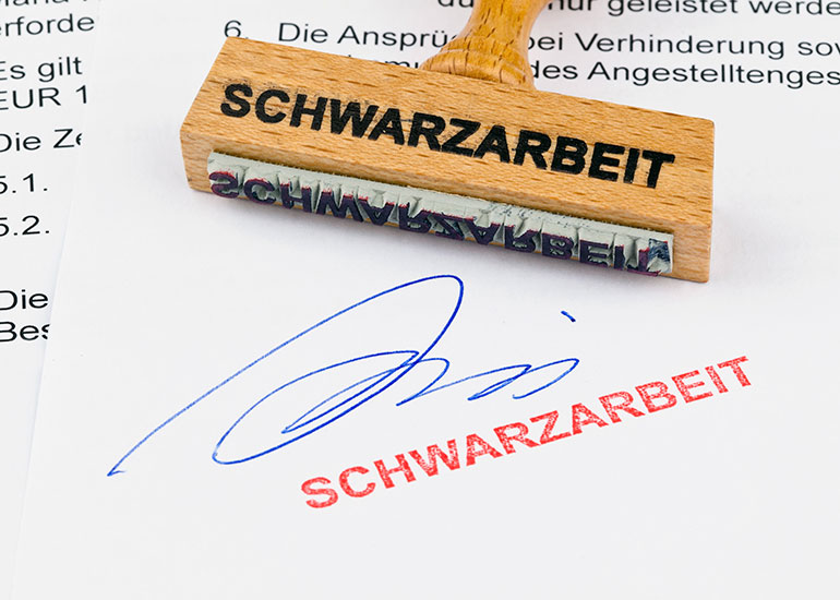 Stempel mit Aufdruck "Schwarzarbeit". Darunter liegt ein bereits gestempeltes Blatt Papier.