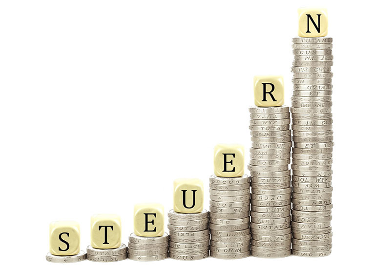 Nach rechts ansteigende Münzstapel. Auf jedem Stapel liegt ein Würfel, die zusammen das Wort "Steuern" ergeben. 