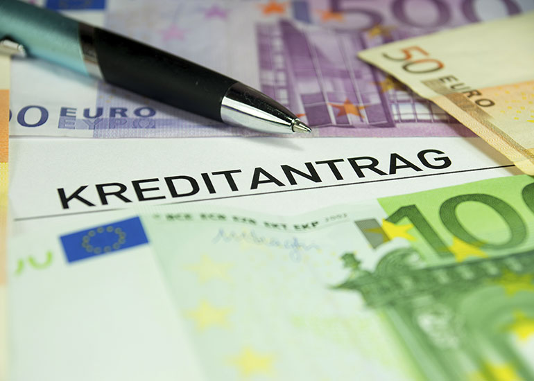 Auf einem Tisch liegen Euro-Banknoten neben einem Kreditantrag und einem Kugelschreiber.