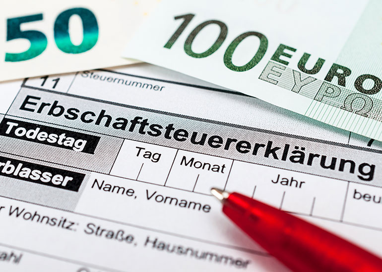 Ein Kugelschreiber liegt auf einer Erbschaftssteuererklärung. Daneben liegen Euro-Banknoten.