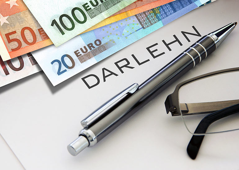 Detailansicht eines Blattes mit dem Text "Darlehn". Daneben liegen Euro-Banknoten, ein Kugelschreiber und eine Brille.