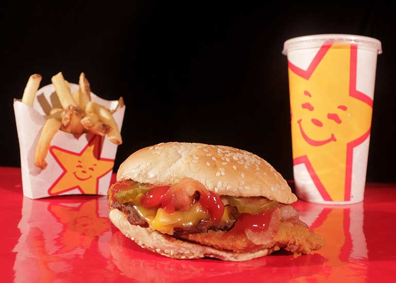Zu sehen sind ein Burger, Pommes frites in einem Pappbecher sowie ein Getränk in einem Pappbecher.