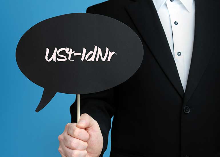 Eine Person im Anzug hält ein Schild mit der Aufschrift „USt-IdNr.” hoch. Das steht für „Umsatzsteuer-Identifikationsnummer”.