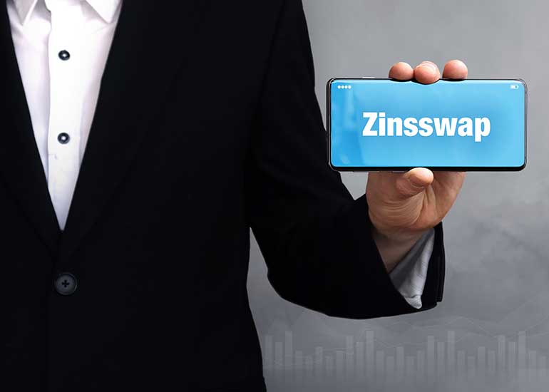 Eine Person in einem Anzug häll ein Mobiltelefon in der Hand auf dem der Text "Zinsswap" zu lesen ist.