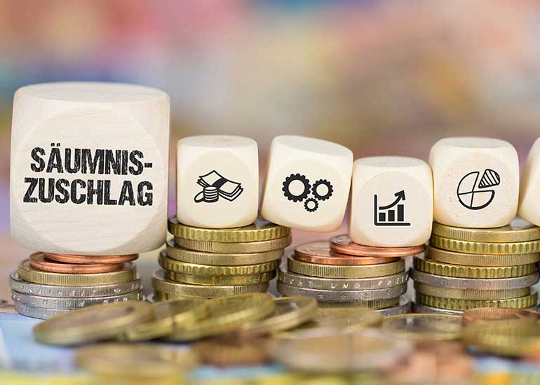 Auf einem Würfel steht „Säumniszuschlag“. Daneben liegen Würfel mit Steuersymbolen. Die Würfel liegen auf Münzstapeln.