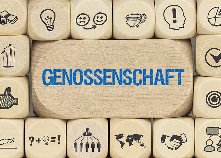 Ein großer Baustein mit der Aufschrift „Genossenschaft“. Darum herum liegen kleinere Bauklötze mit Symbolen wie z.B. Handschlag, Geldscheine und Münzen, einem Pfeil in der Mitte einer Zielscheibe und Glühbirnen.