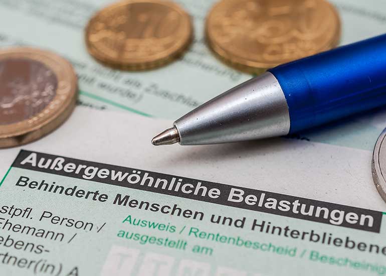 Detailansicht eines Formulars. Zu sehen ist der Text „Außergewöhnliche Belastungen”. Darauf liegen ein Kugelschreiber und Münzen.