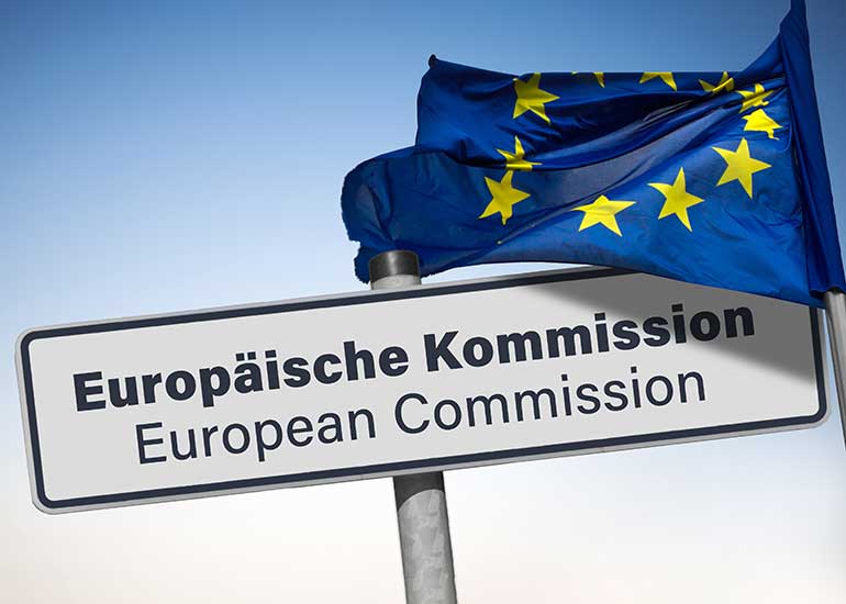 Auf einem Schild steht „Europäische Kommission/European Commission”. Daneben ist eine Europaflagge an einem Fahnenmast zu sehen.